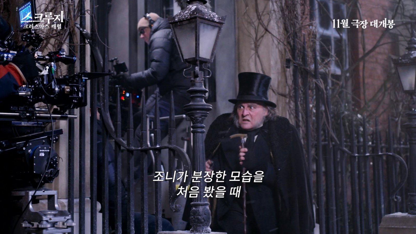 映画『スクルージ:クリスマス・キャロル』の撮影現場でスクルージ姿のジョニー・デップが立つ場面。画面には11月劇場公開の告知がある