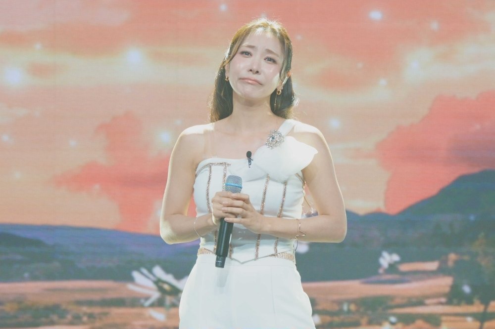 白いドレス姿でマイクを持ち、歌唱中に涙を浮かべるイ・ソナ