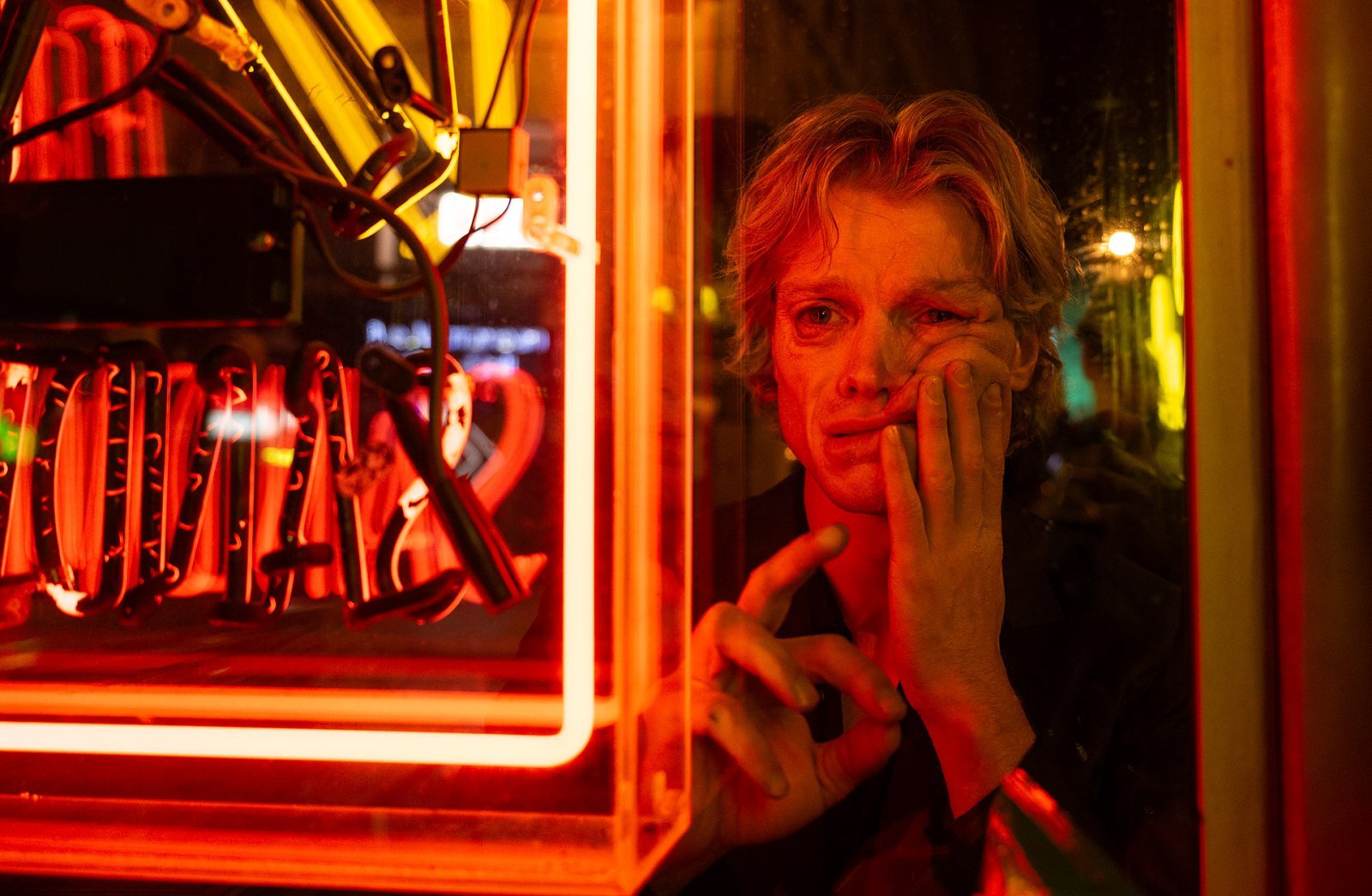 赤い照明の室内で頬に手を当てる映画『クレイフェイス』のマット・ヘイガン