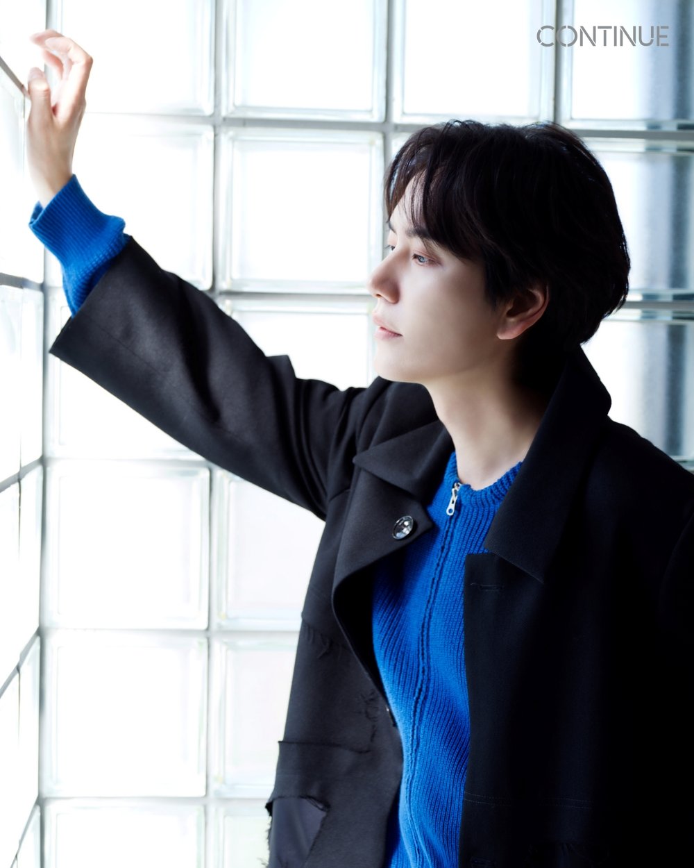青いセーターと黒いコート姿で窓辺に立つキュヒョン。EP『CONTINUE』のロゴが添えられている