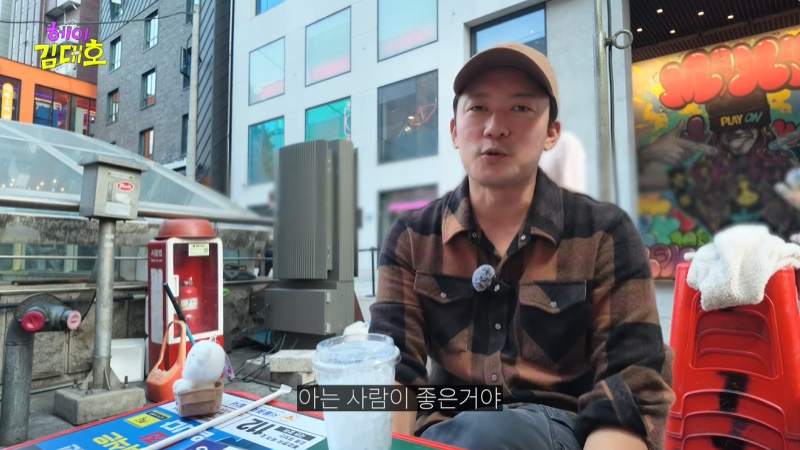 YouTube動画でキャップをかぶり、屋外のテーブルで話すキム・デホ