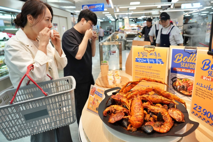 롯데마트가 업계 최초로 델리 신상품 정식 출시 전 고객 의견을 반영하는 '파일럿 키친'을 운영한다. 고객들이 제타플렉스 잠실점에서 첫 테스트 상품인 '보일링 씨푸드'를 맛보고 있다. /사진=롯데마트