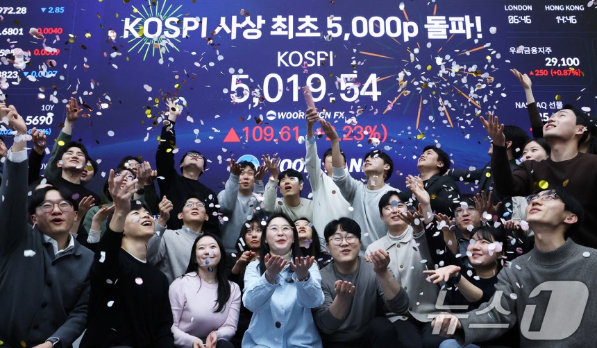 한국 증시가 사상 처음으로 '코스피 5000' 쾌거를 달성한 22일 서울 중구 우리은행 본점 딜링룸에서 직원들이 장중 최고가가 찍힌 전광판을 배경으로 코스피 5000 돌파를 축하하고 있다.이날 코스피는 이재명 대통