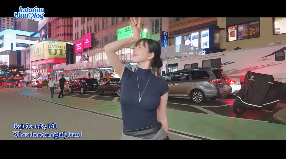 ニューヨークの街角で腕を上げ「All That Jazz」の歌詞を口ずさむカリナ