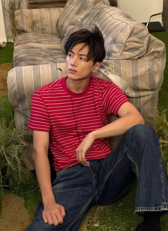 赤いボーダーTシャツと濃紺のジーンズ姿でソファに座るENHYPENのジェイ