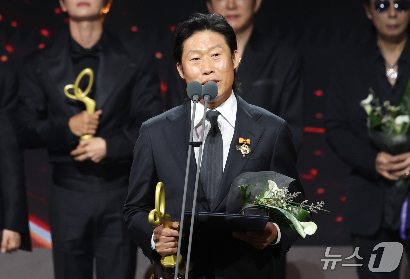 大統領表彰を受けたユ・ヘジンが、花束と表彰のトロフィーを持ってステージ上で受賞コメントを述べる