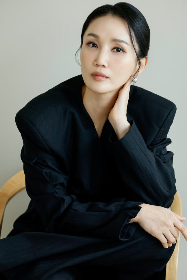 黒い衣装で椅子に座り、こちらを見る俳優パク・ボギョン