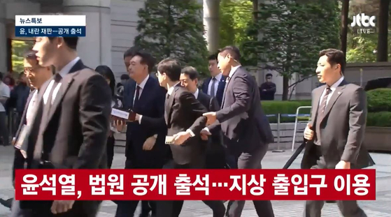 내란 우두머리 혐의로 재판을 받는 윤석열 전 대통령이 12일 법원에 공개 출석하는 과정에서 경호원이 질문하는 취재진의 팔을 잡아끌어 제지하고 있다.〈사진=JTBC 방송화면 캡처〉