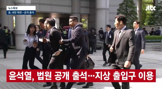 내란 우두머리 혐의로 재판을 받는 윤석열 전 대통령이 12일 법원에 공개 출석하는 과정에서 경호원이 질문하는 취재진의 팔을 잡아끌어 제지하고 있다.〈사진=JTBC 방송화면 캡처〉