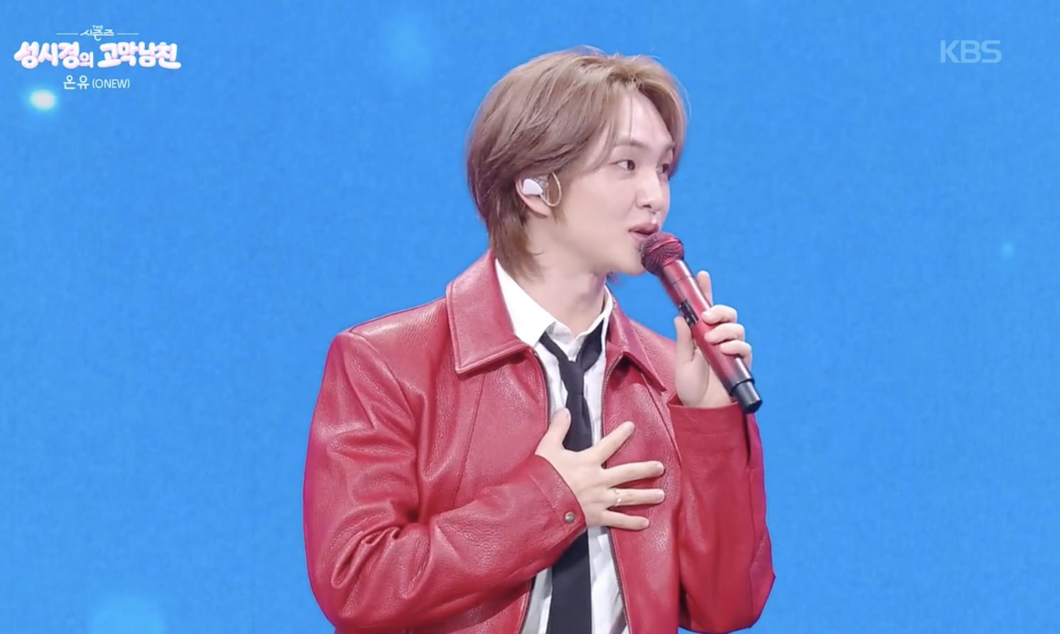 KBSの音楽番組で赤いジャケットを着てマイクを持つSHINeeのオンユ。