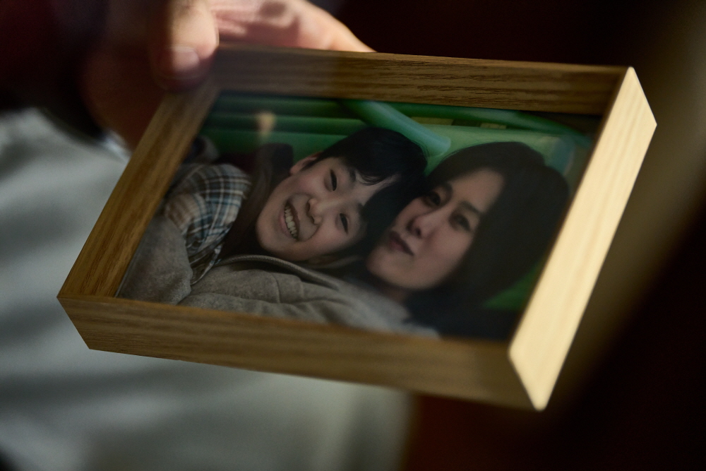 映画『失楽園』の一場面。母と幼い息子が写った写真立てを手に取る