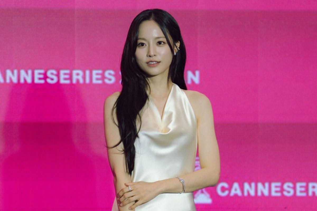 白いノースリーブの衣装を着たペ・ユンギョンが、カンヌ国際シリーズフェスティバルのロゴを背に立つ