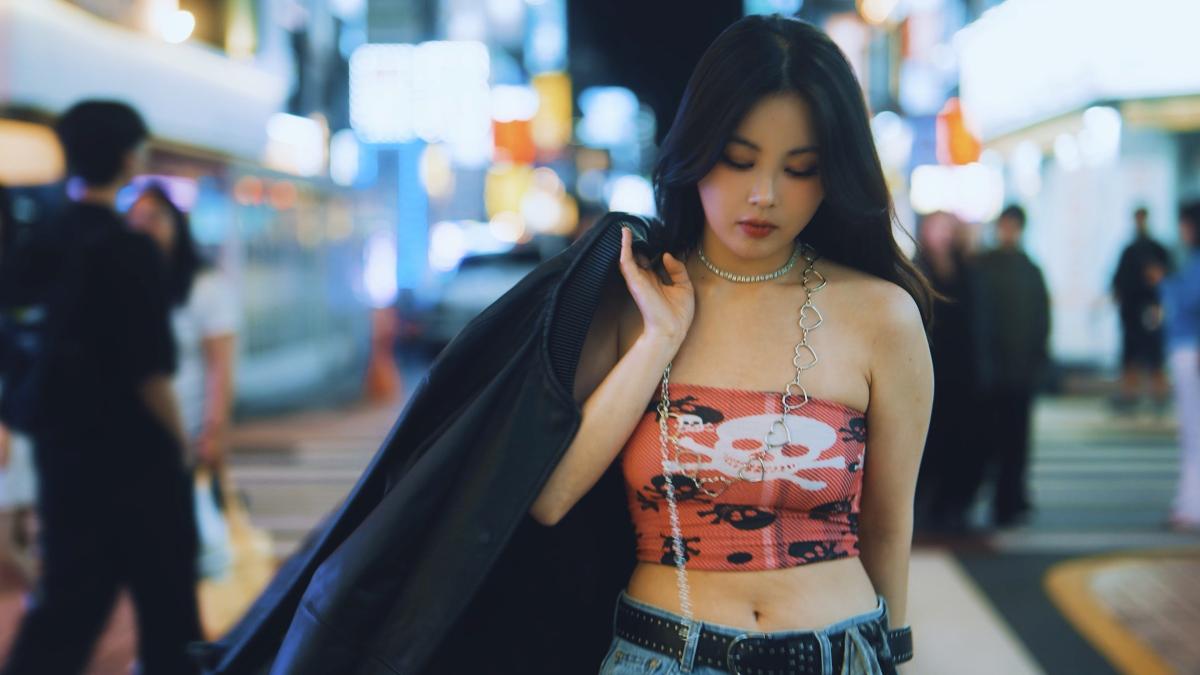 夜の街で、オレンジ柄のトップスに黒いジャケットを羽織った女性