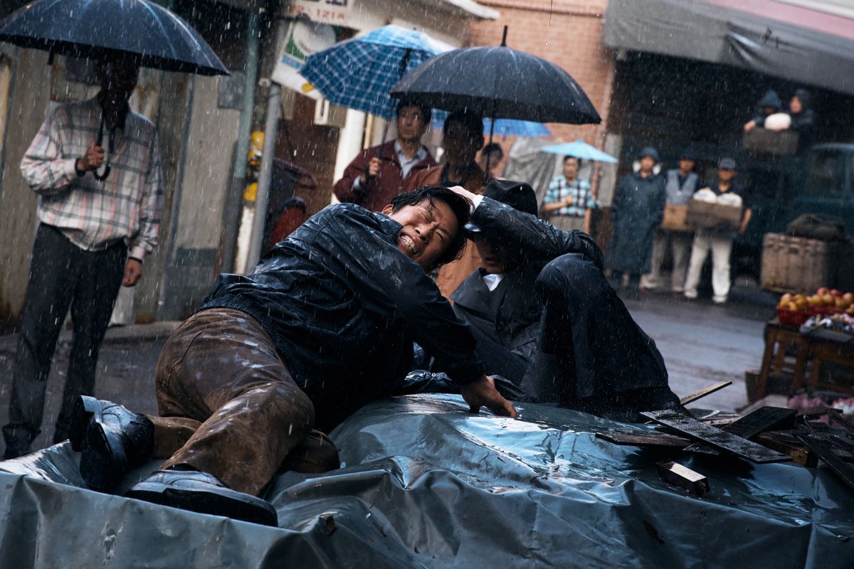 映画『暗殺者たち』の雨の中の場面。倒れた男性を別の男性がかばうようにしている