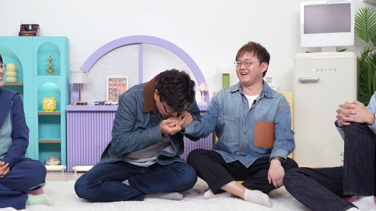 KBS2『屋上部屋の問題児たち』のセットで、男性出演者が隣に座る男性の手へ顔を寄せる場面
