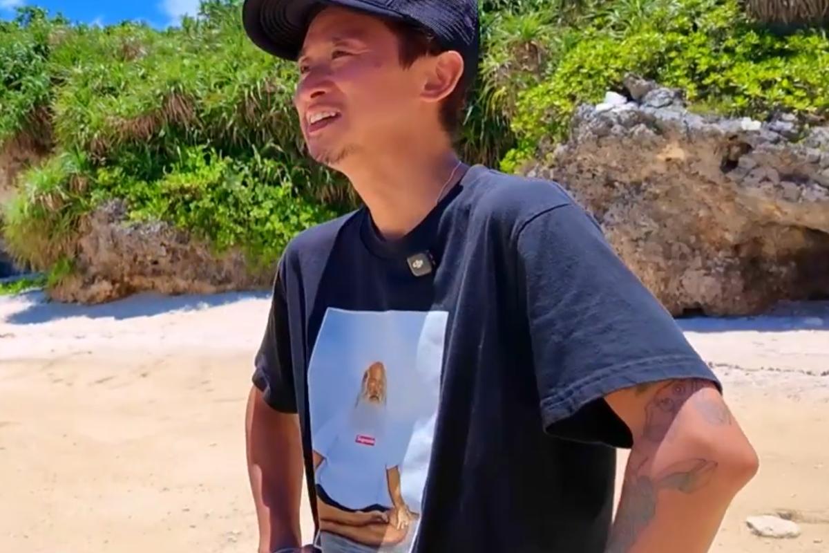 沖縄の海辺で、左腕にタトゥーが見えるTシャツ姿の大野智