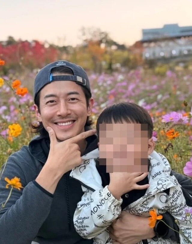 花畑で息子を抱き、笑顔を見せるチェ・フィリップ。息子の顔にはぼかしが入っている