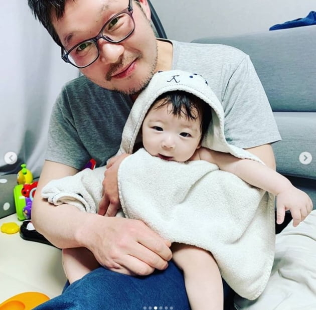 ユ・ジェミョンが幼い息子を抱き、カメラに笑顔を向けている。