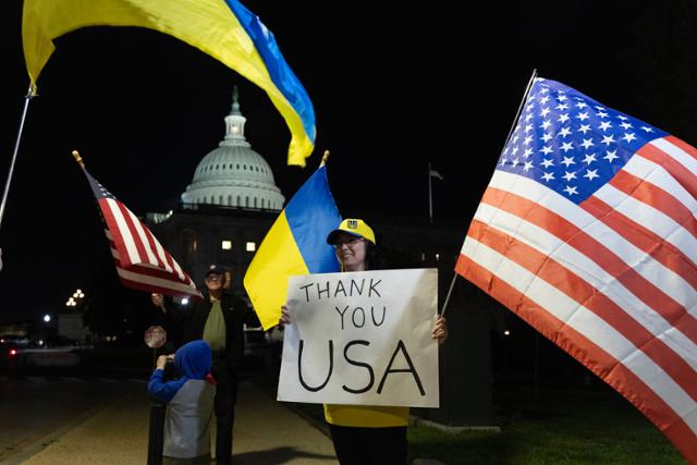23일 대우크라이나 지원안이 포함된 953억 달러 규모의 대외 안보 패키지 법안이 미국 상원을 통과한 뒤 우크라이나 지지자들이 미 워싱턴 국회의사당 앞에서 양국 국기와 손팻말을 들고 미국에 감사의 뜻을 전하고 있다.