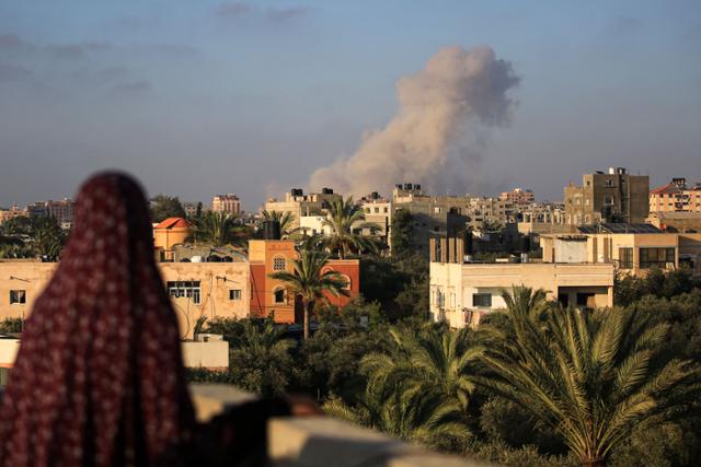한 팔레스타인 여성이 11일 가자지구 중부 알 자와이다에서 이스라엘 공습을 받아 연기가 피어오르는 가자시티를 바라보고 있다. 알 자와이다=AFP 연합뉴스