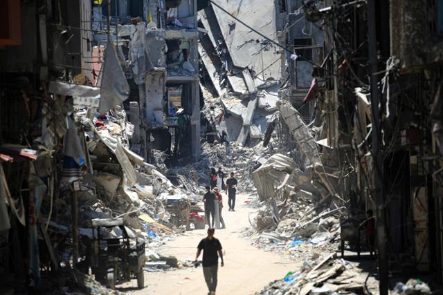 팔레스타인 사람들이 11일 가자지구 남부 칸유니스에서 이스라엘 공습으로 파괴된 건물 사이를 걷고 있다. 칸유니스=AFP 연합뉴스