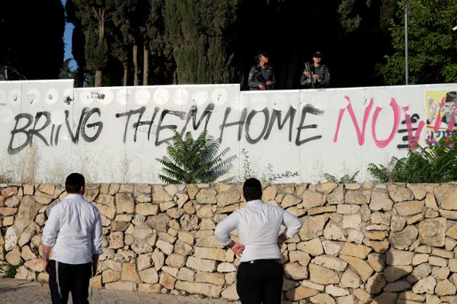 이스라엘 시민들이 17일 예루살렘에서 반정부 시위대가 담장에 적은 '그들을 당장 집으로 데려오라(Bring Them Home Now)'는 문구를 보고 있다. 시위대는 팔레스타인 무장 정파 하마스에 억류된 인질들의 석