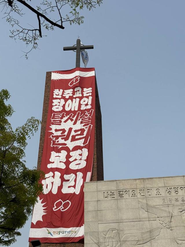 지난달 18일 서울 종로구 혜화동성당 종탑에 전국장애인차별철폐연대 활동가들이 장애인의 탈시설 권리를 보장하라고 쓴 현수막이 걸려 있다. 활동가 2명은 이날부터 고공농성에 들어갔다. 연합뉴스.