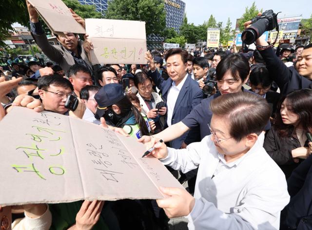 민심을 청취하는 '경청 투어'에 나선 이재명 더불어민주당 대선 후보가 7일 전북 전주시 완산구 풍남문 인근에서 공판 연기를 환영하는 지지자의 응원 피켓에 사인을 해주고 있다. '공판 연기 환영, 대통령은 국민이 뽑습