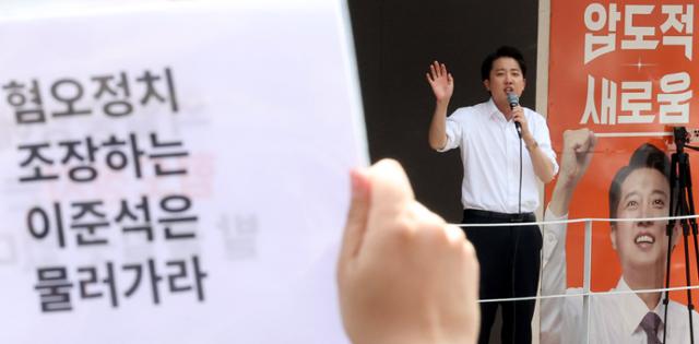지난달 30일 서울 동작구 중앙대 후문에서 유세 발언을 하고 있는 이준석 개혁신당 대선 후보를 향해 한 대학생이 '혐오정치 조장하는 이준석은 물러가라'는 문구를 적은 피켓을 들어 보이고 있다. 뉴시스