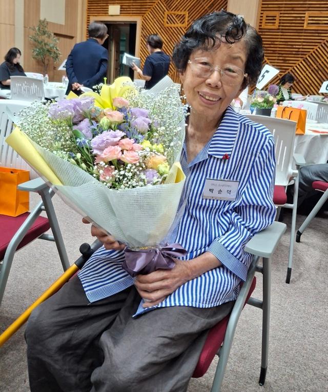 11일 전북 전주 치명자산성지 평화의전당 유항검홀에서 열린 '희망2025캠페인 유공자 시상식'에서 폐지 등을 모아 장학금을 기부한 박순덕(90) 할머니가 꽃다발을 들고 앉아 있다. 정읍시 제공