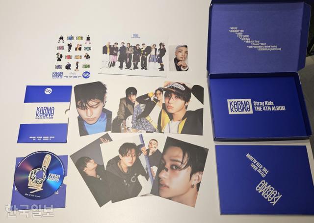 그룹 스트레이키즈 4집 음반 '카르마' 일반반의 '세레모니' 버전을 개봉해봤다. 얇은 플라스틱 포장재, 종이 박스, 112쪽 분량의 포토북, 엽서 세트, 미니 포스터, 종이로 만든 CD집, 코팅이 된 스티커와 포토카