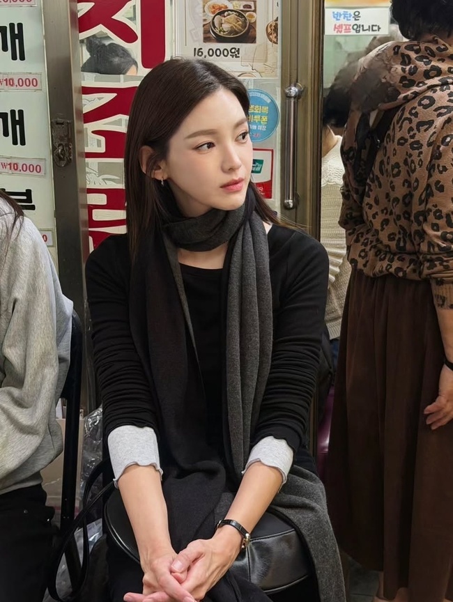 南大門市場の店内で黒い服とグレーのマフラーを身に着け、椅子に座るチョン・ガウン。