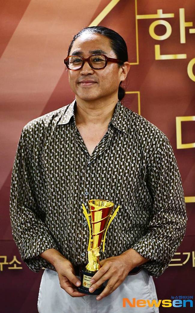 韓国映画監督のキム・ハンミン。ニュースエンの取材時にトロフィーを手にしている