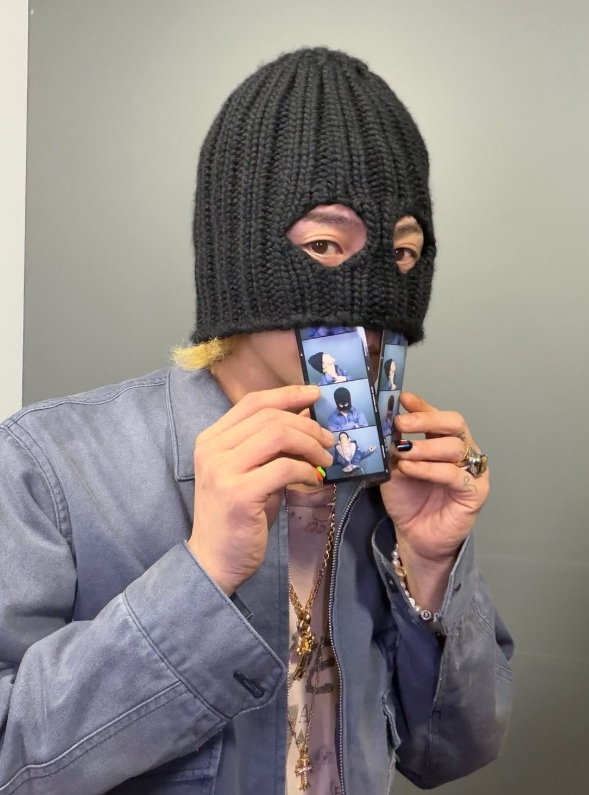 目元だけ見える黒いビーニーをかぶり、プリクラ写真を手にするG-DRAGON