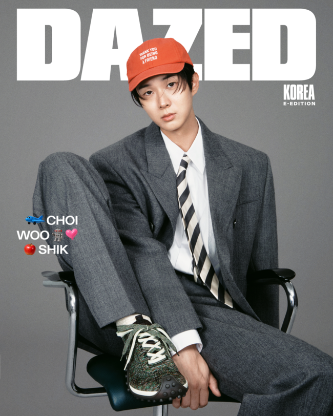 グレーのスーツと赤いキャップを合わせ、椅子に腰掛けるチェ・ウシク。Dazed Koreaのロゴが入ったファッション写真。