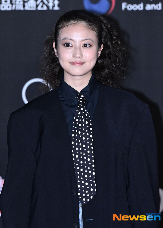 黒いジャケットと水玉模様のネクタイ姿で微笑む今田美桜