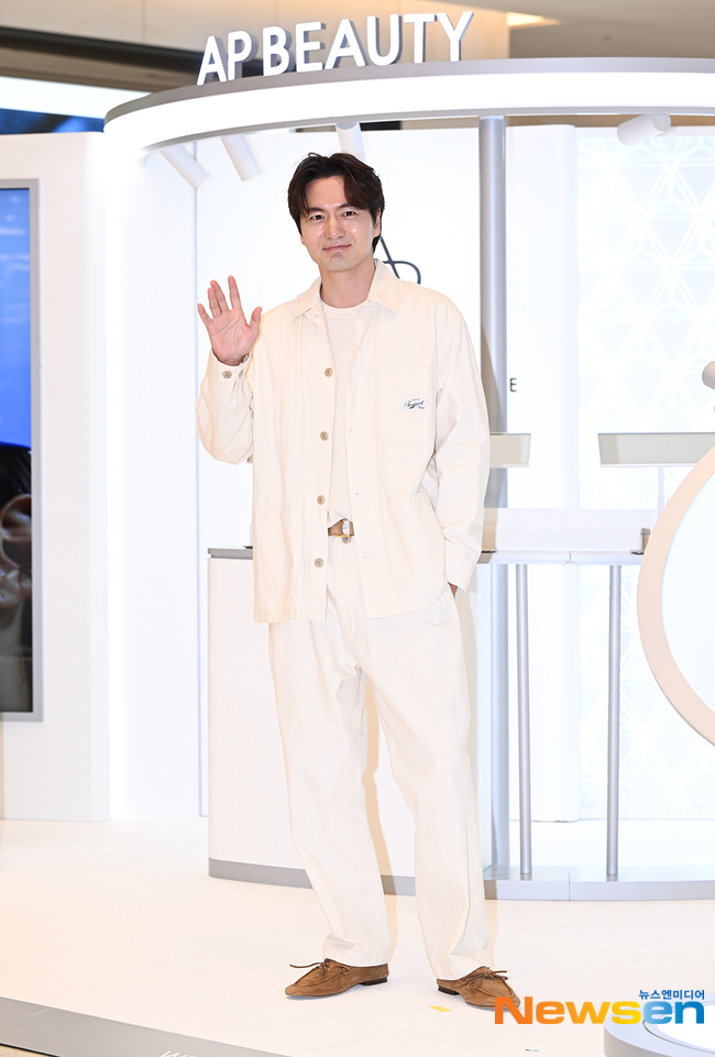 AP BEAUTYのサインを背に、白のシャツとパンツ姿で手を挙げるイ・ジヌク