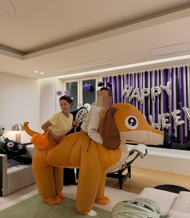 ハン・ジヘのハロウィーン会の写真。犬の着ぐるみ姿の人物と、カオナシの小道具を持つ女性が飾り付けた部屋にいる