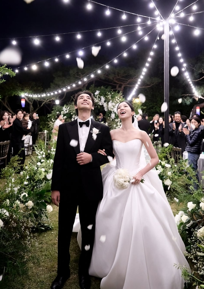 屋外の結婚式で、黒いタキシード姿のソン・ジホと白いウェディングドレス姿のキム・ソリが並ぶ