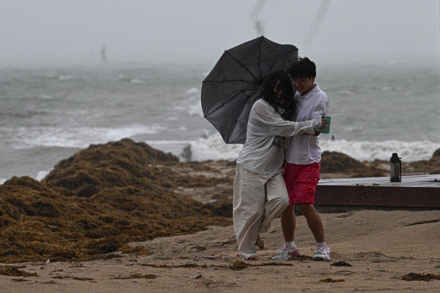 Tourists are seen in the wind and rain at Tanmen central fishing port in Qionghai, south China's Hainan Province, on Jul