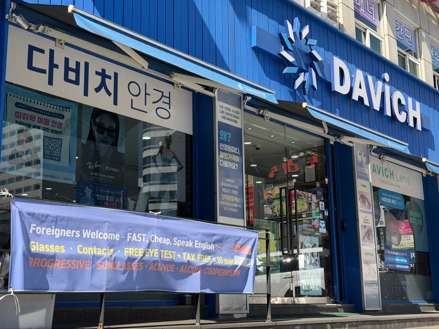 A placard advertising that foreigners are welcome and that staff speak English hangs in front of a Davich Optical branch